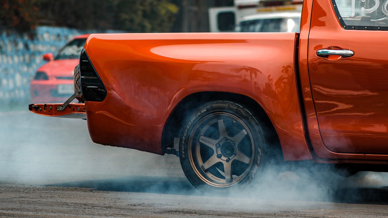 A vibrant orange car performing a drift on a race track with smoke trailing from its tires (Pexels photo)